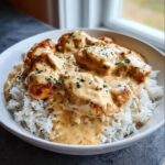A white bowl filled with white rice topped with pieces of golden chicken covered in a thick, creamy sauce, garnished with parsley, ready for Creamy Smothered Chicken and Rice.