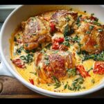 Four crispy-skinned Creamy Tuscan Chicken Thighs simmering in a rich, creamy sauce with spinach and sun-dried tomatoes.