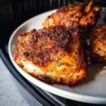 Close-up of perfectly cooked, crispy Air Fryer Chicken Thighs with a seasoned, browned skin on a white plate.