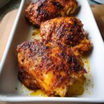 Three perfectly seasoned Crispy Baked Chicken Thighs with golden-brown, spiced skin resting in a white serving dish.