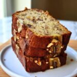 Three stacked slices of moist Greek Yogurt Banana Bread topped with walnuts and banana pieces.