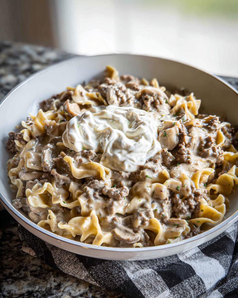 A hearty bowl of Ground Beef Stroganoff mixed with egg noodles and mushrooms, topped with a dollop of sour cream.