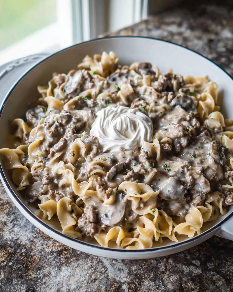 A creamy bowl of Ground Beef Stroganoff served over wide egg noodles, topped with sour cream.