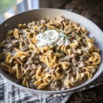 A skillet full of creamy Ground Beef Stroganoff mixed with egg noodles and topped with sour cream and parsley.