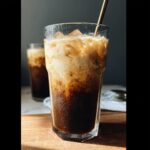 Close-up of an Iced Brown Sugar Oatmilk Shaken Espresso with creamy foam swirling into dark coffee.