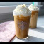 Close-up of a tall glass of Iced White Chocolate Mocha topped with whipped cream and white chocolate shavings.