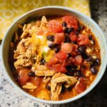 A bowl of shredded chicken chili topped with black beans, diced tomatoes, cheese, and sour cream, perfect for Instant Pot Weeknight Winners.