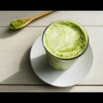 A vibrant green Matcha Green Tea Latte in a glass, with matcha powder on a wooden spoon nearby.