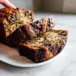 Two thick slices of moist Chocolate Chip Banana Bread with melted chocolate drizzled on top.