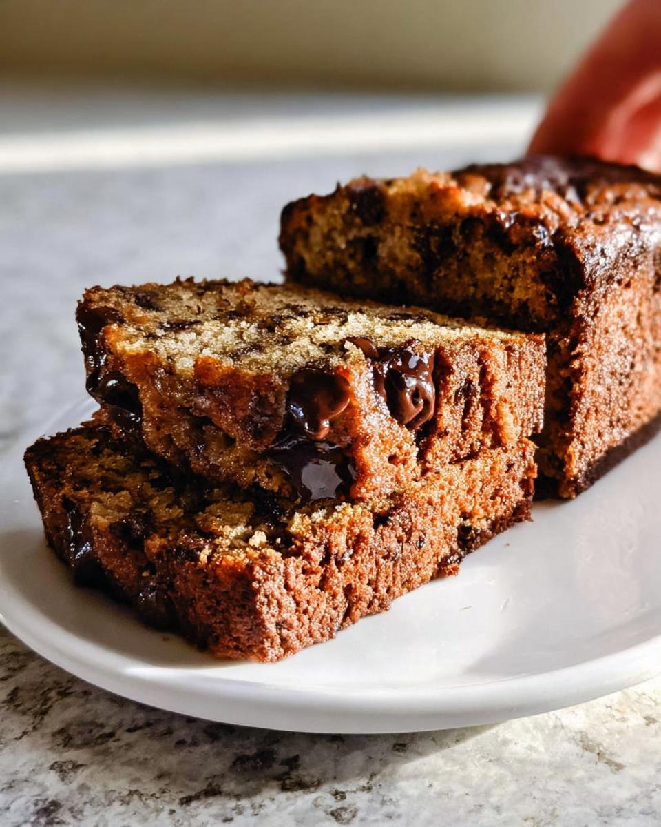 Close-up of three moist slices of Chocolate Chip Banana Bread stacked on a white plate, showing melted chocolate chips.
