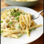 A fork lifts creamy pasta, chicken, and peas from a plate of One-Pot Chicken Alfredo.