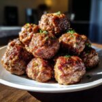 A close-up stack of juicy, browned Oven-Baked Meatballs garnished with fresh parsley on a white plate.