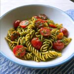 A close-up of Pesto Pasta with Cherry Tomatoes, featuring fusilli coated in green pesto and topped with halved, bright red cherry tomatoes.