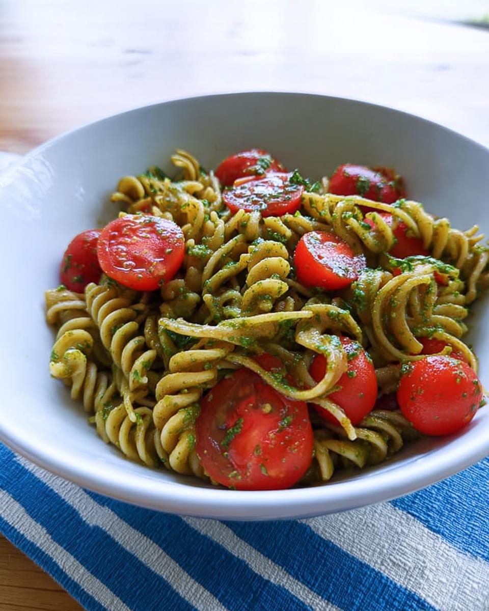 A close-up of Pesto Pasta with Cherry Tomatoes, featuring fusilli coated in green pesto and halved bright red tomatoes.