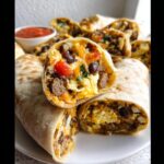 A close-up of a cut Protein-Packed Breakfast Burrito showing eggs, sausage, cheese, and black beans.