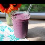 A vibrant purple smoothie in a glass jar with a straw, sitting on a wooden surface next to sunflowers. Perfect for 5-Ingredient Smoothie Packs.