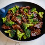 A close-up overhead view of glossy, saucy Beef & Broccoli Skillet served hot in a dark skillet.