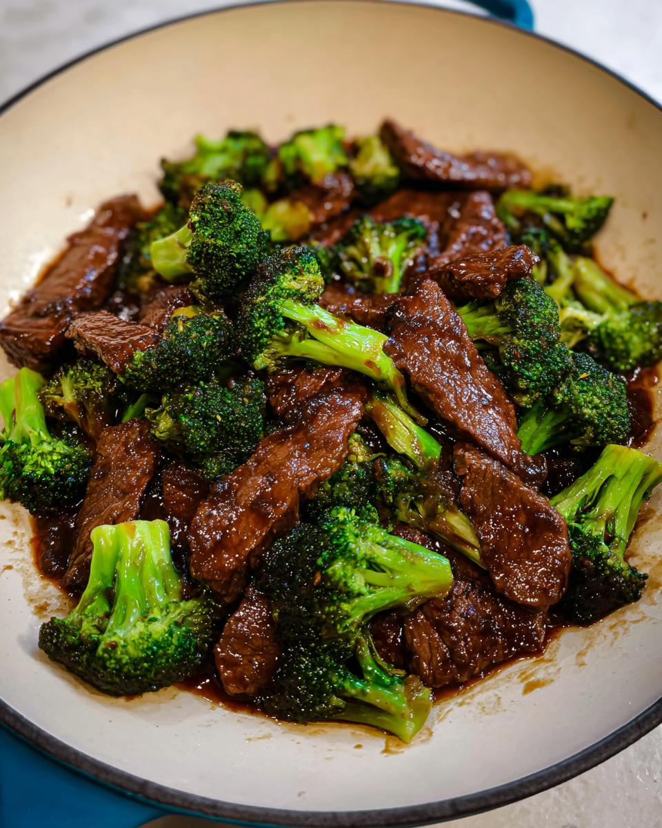 Close-up of tender strips of beef coated in dark sauce mixed with bright green broccoli florets in a skillet.