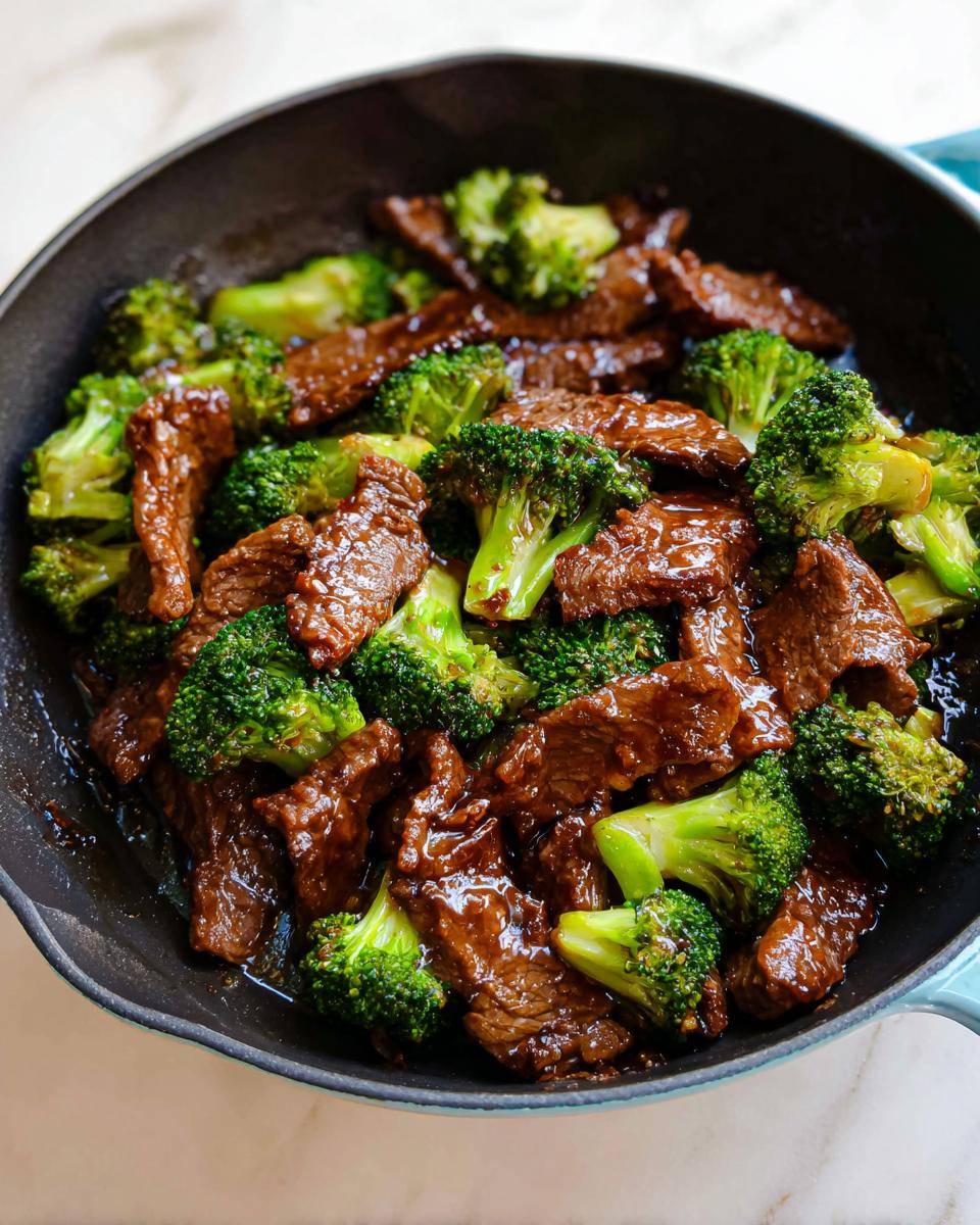 Close-up of glossy, saucy Beef & Broccoli Skillet mixture cooking in a dark cast iron pan.