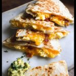Close-up of stacked, quartered Breakfast Quesadillas filled with scrambled eggs, bacon bits, and melted cheddar cheese.