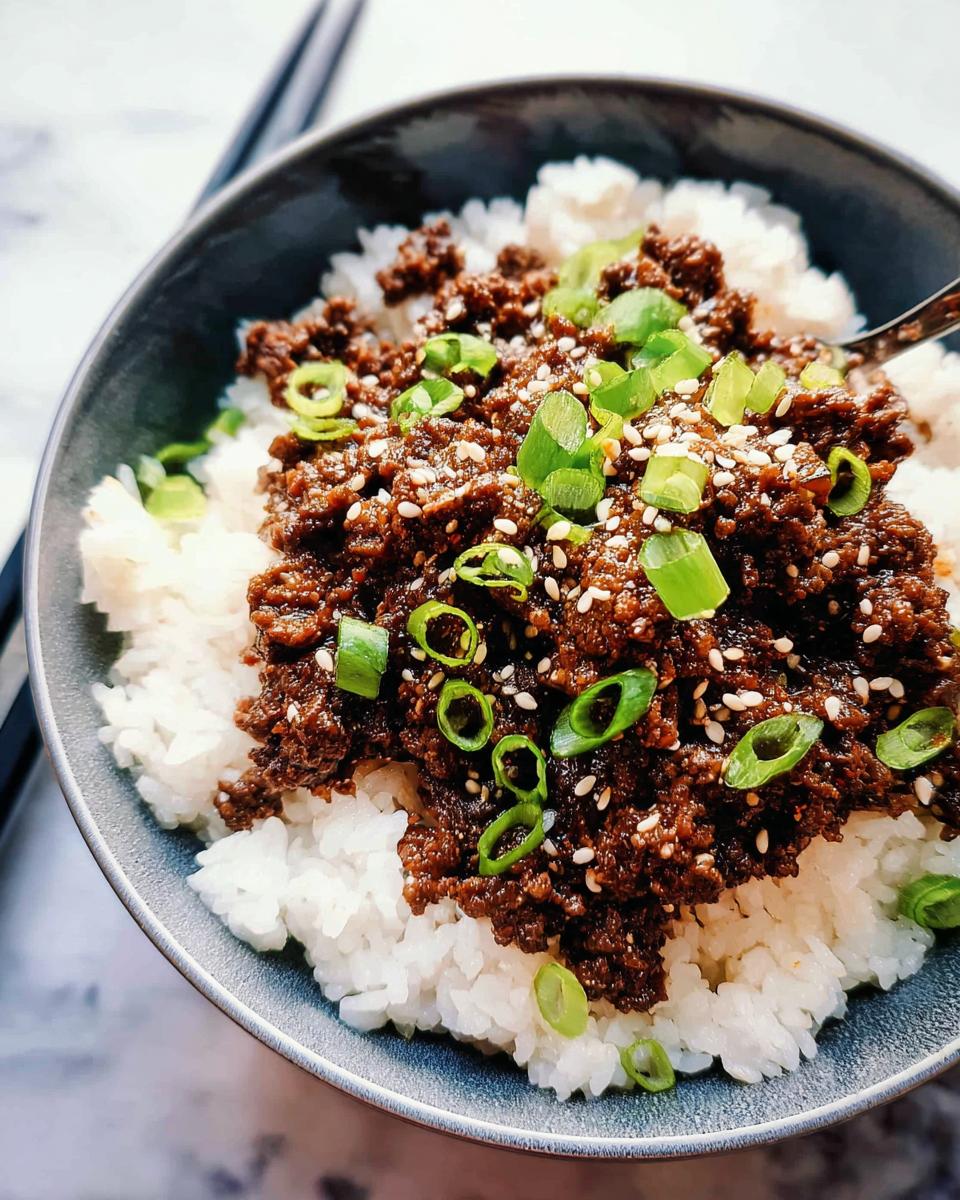 Close-up of a bowl of Korean Ground Beef Bowls (Quick) served over white rice, topped with green onions and sesame seeds.