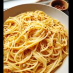 A close-up, appetizing shot of perfectly coated Spaghetti Aglio e Olio, garnished with red pepper flakes.
