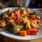 Close-up of seasoned chicken pieces mixed with roasted broccoli and red peppers from a Sheet Pan Chicken & Veggie Dinner.