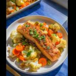 A perfectly cooked fillet of Sheet-Pan Salmon & Veg served on a white plate with roasted cauliflower, carrots, and green olives.