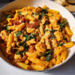 Close-up of a bowl filled with Showstopper Chicken and Pasta Delight, featuring creamy sauce, spinach, and sun-dried tomatoes.