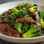 Close-up of tender beef strips coated in savory sauce mixed with bright green broccoli florets in a white bowl.