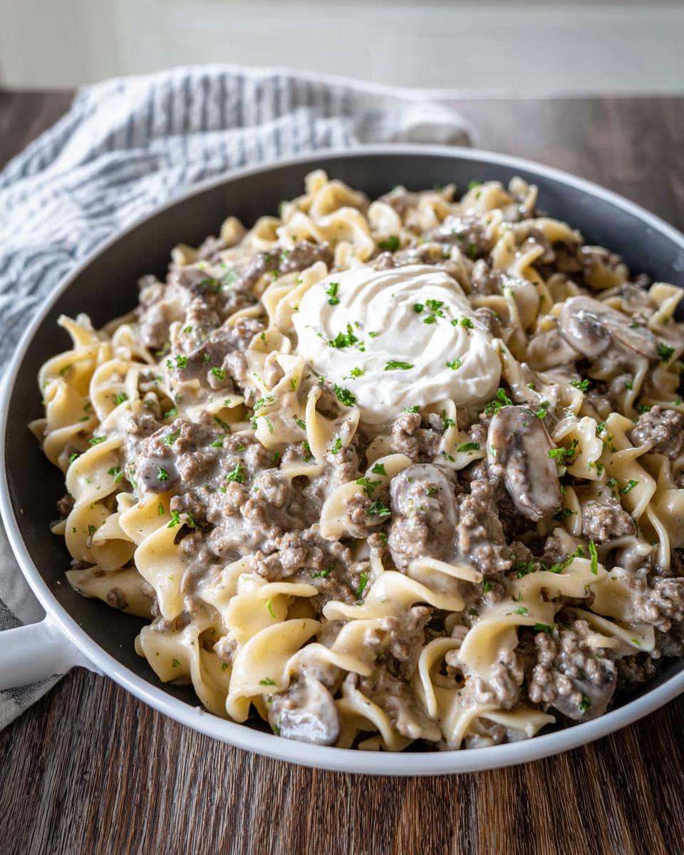 A skillet filled with creamy Ground Beef Stroganoff mixed with egg noodles and mushrooms, topped with sour cream.