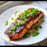 Close-up of a perfectly cooked Soy-Ginger Glazed Salmon fillet served over white rice and topped with sesame seeds and green onions.