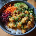 A close-up of a Bang Bang Chicken Bowl with crispy chicken, rice, avocado, shredded carrots, and red cabbage.