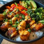 A close-up of a Crave-Worthy Bang Bang Chicken Bowl with crispy chicken, rice, broccoli, carrots, avocado, and a creamy sauce.