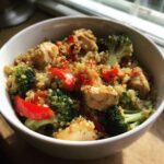 A close-up of a white bowl filled with chicken, quinoa, broccoli, and red bell peppers, perfect for easy meal prep recipes.