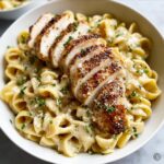 A bowl of Creamy Garlic Parmesan Chicken Pasta topped with sliced grilled chicken and fresh parsley.