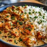 A close-up of Creamy Creamy Smothered Chicken and Rice, with tender chicken pieces in a rich sauce served alongside fluffy white rice and garnished with parsley.