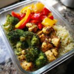 A clear glass container filled with an Easy Healthy Meal Prep for the Week: seasoned chicken breast, steamed broccoli, bell peppers, and quinoa.
