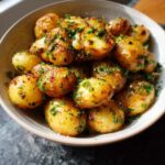 A bowl filled with golden-brown, crispy garlic herb roasted baby potatoes, generously sprinkled with fresh parsley.