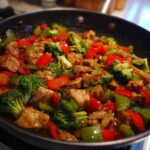 Close-up of a healthy beef and broccoli stir-fry in a pan, featuring tender beef, vibrant broccoli florets, and red and green bell peppers.