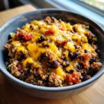 A close-up of a hearty quinoa bowl with ground beef, black beans, tomatoes, and melted cheese, representing easy high-protein meals.