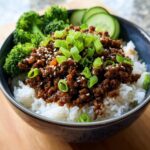 A delicious Korean ground beef bowl served over white rice, with steamed broccoli and cucumber slices, topped with green onions and sesame seeds.