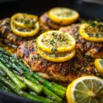 A close-up of a delicious low-calorie dinner featuring lemon herb chicken breasts with roasted asparagus, garnished with lemon slices and fresh herbs.