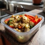 A clear plastic container filled with a healthy make-ahead lunch or dinner idea: chicken, quinoa, broccoli, carrots, and red peppers.