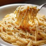 A fork lifting a swirl of One Pot Creamy Garlic Pasta coated in a rich, cheesy sauce and sprinkled with parsley.