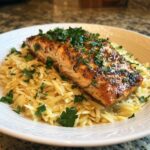 A perfectly seared salmon fillet sits atop a bed of creamy lemon orzo, garnished with fresh parsley.