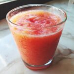A close-up of a glass filled with vibrant strawberry peach juice, showing its frothy texture.