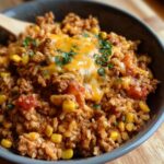 A close-up of a bowl filled with bold turkey taco meat, rice, corn, tomatoes, and melted cheese, garnished with parsley.