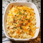 A delicious Cheesy Chicken and Rice Bake in a white casserole dish, topped with melted cheddar cheese and parsley.