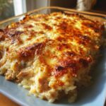 A close-up of a golden-brown cheesy chicken and rice bake in a baking dish, showing melted cheese and tender chicken.